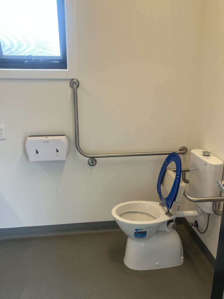 Accessible toilet with grab rails, back rest and ample floor space surrounding