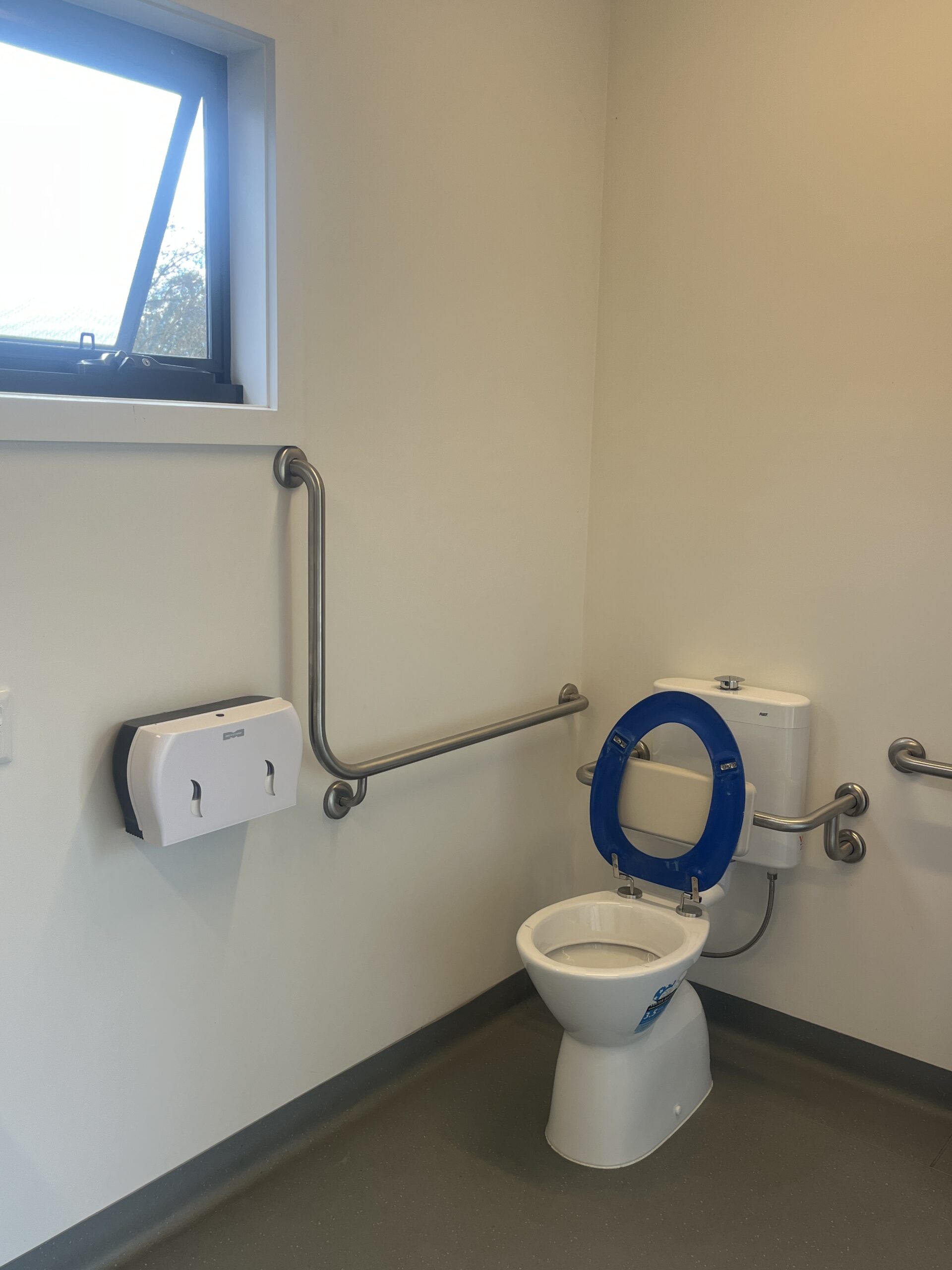 Accessible toilet with grab rails, back rest and ample floor space surrounding